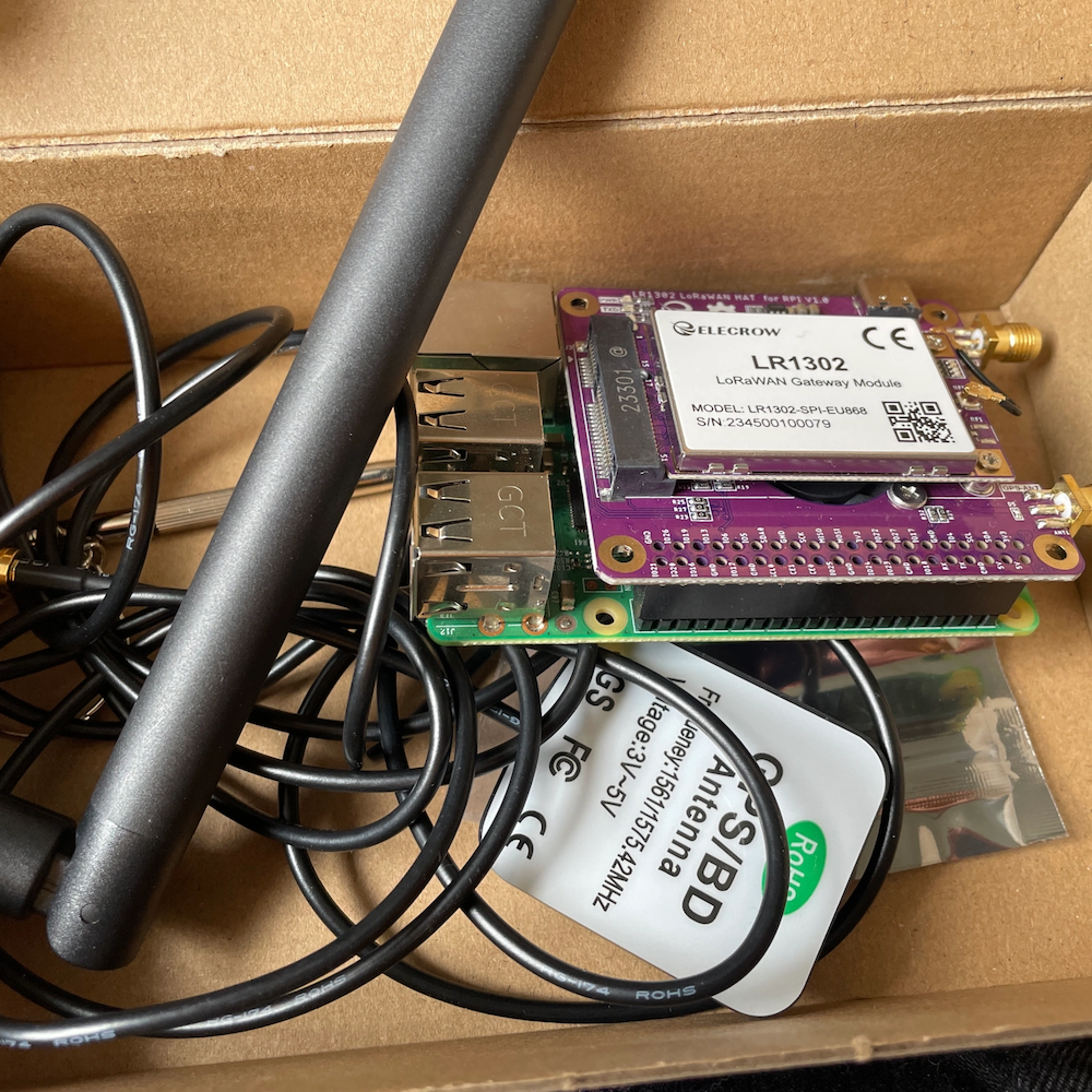 A jumble of wires, a lora hat and a raspberry pi in a cardboard box