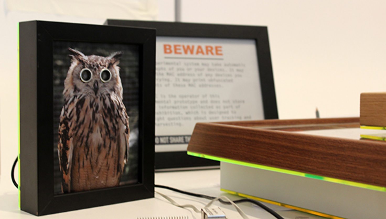 A picture of an owl in a frame with ultrasonic sensor eyes and a part visible warning sign that you are being watched and your data is being collected by the installation