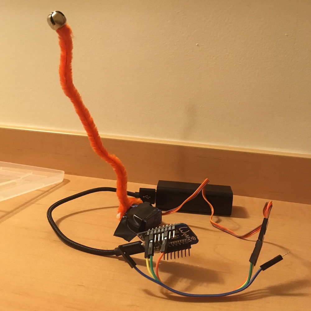 An orange pipecleaner connecetd to a motor and via wifi to a slack channel